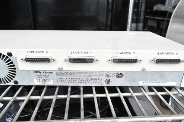 SynOptics LattisHub 2814, rear view showing five expansion ports and compliance labels, in used condition on a metal rack.