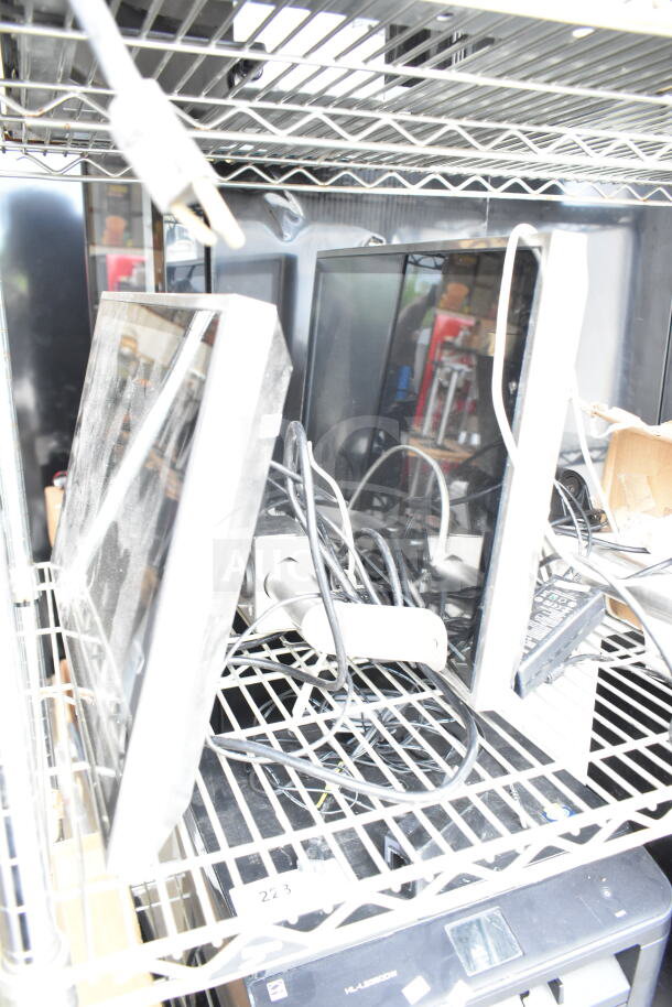 Various POS monitors and printers, including Epson and Dell models, on metal shelving with visible cables. Mixed condition.