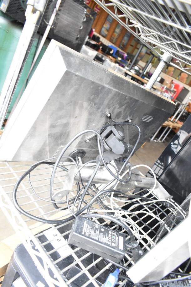 5 various items including POS monitors and receipt printers on a metal shelf, showing cords and power adapters.