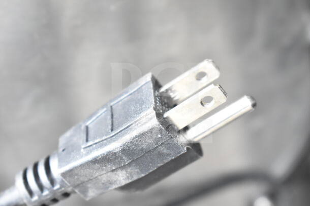 Close-up of a two-prong electrical plug, part of auction lot with POS monitors and receipt printers.