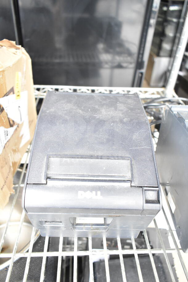 Dell receipt printer, dusty exterior, on metal shelf; part of a lot including Epson receipt printer and POS monitors.