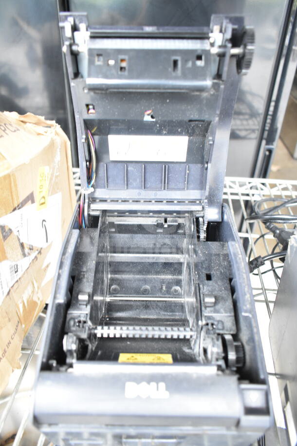 Open Dell receipt printer on metal shelf, showing internal components. Visible wires, used condition. Box with shipping labels nearby.