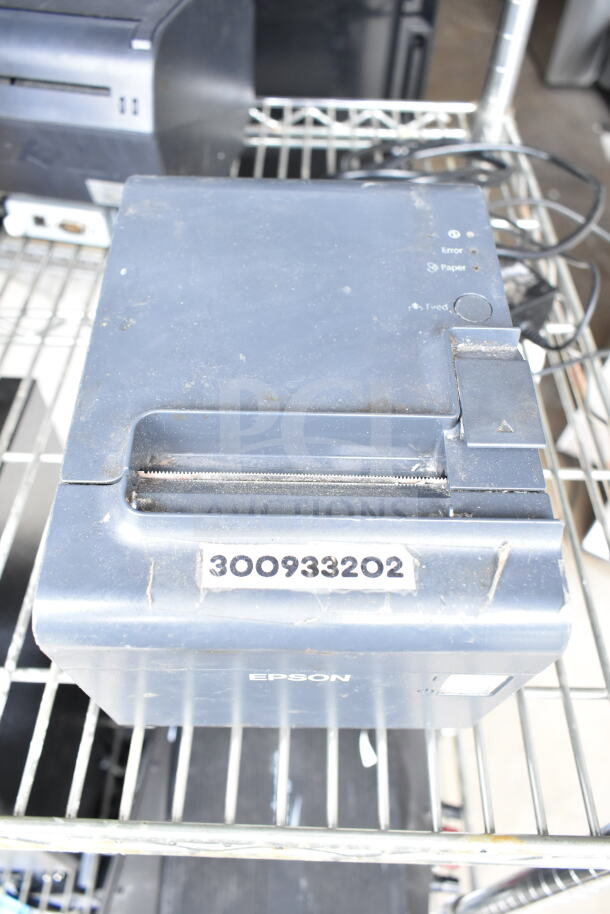 Epson receipt printer with a visible label "300933202." Resting on a wire rack, showing signs of wear.
