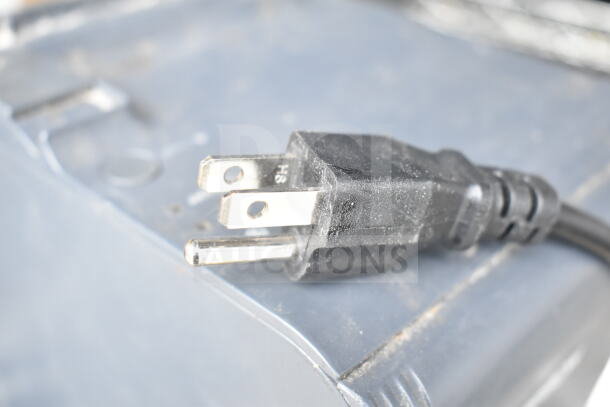 Close-up of a black electrical plug on a grey surface, part of a lot with POS monitors and receipt printers.
