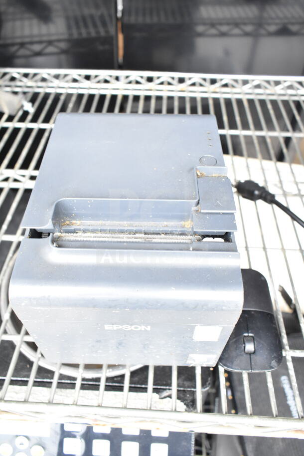 Epson receipt printer, gray, on metal shelving. Shows wear and dust. Includes cable.