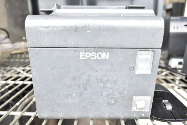 Epson receipt printer, gray, used condition, visible power button, liner-free sticker on metal rack.