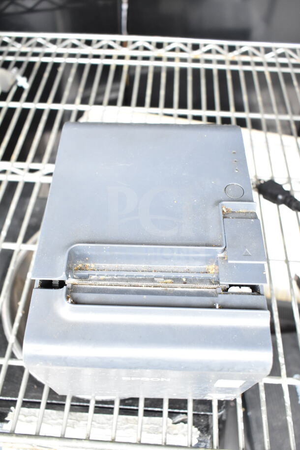Epson receipt printer on metal shelf, showing wear and dust. Suitable for POS systems; a valuable addition for business setups.