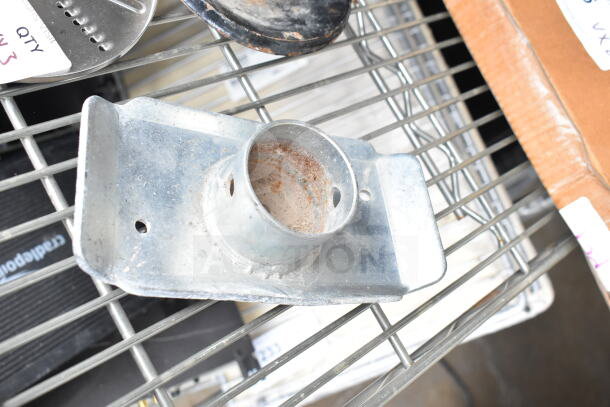 3 various items including a food processor blade, one rusted metal piece, and another metal part on a wire shelf.