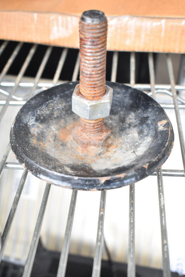 Rusty metal piece with a threaded bolt and round base, in used condition, visible on metal shelving.