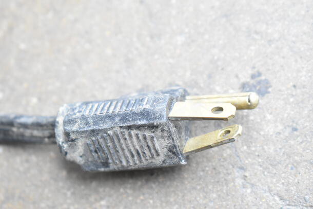 Close-up of a worn, dusty power plug with visible brass prongs on a gray surface.