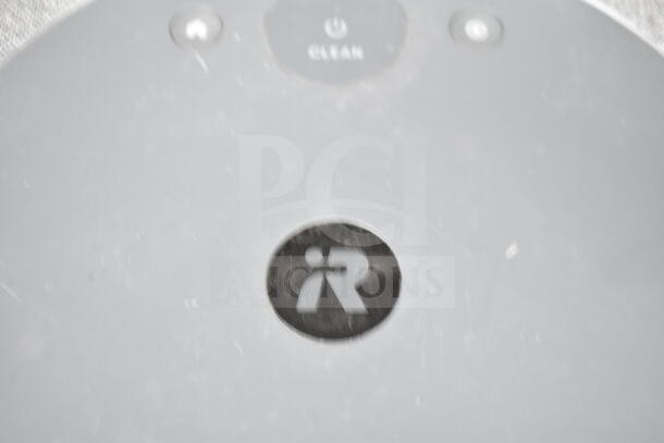 Close-up of a Roomba robot vacuum, featuring the iRobot logo and "CLEAN" button. Slightly worn surface visible.