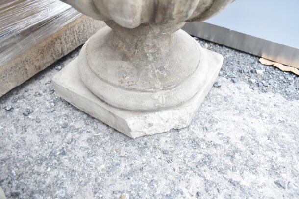 Stone vase with ornate pedestal base; visible wear on base edge; suitable for outdoor decor.