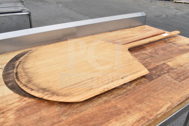 Butcher block table with an under shelf, features wood grain surface and includes pizza peel with burnt markings.