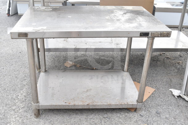 Stainless steel table with under shelf, showing signs of wear and discoloration. Ideal for industrial or kitchen use.