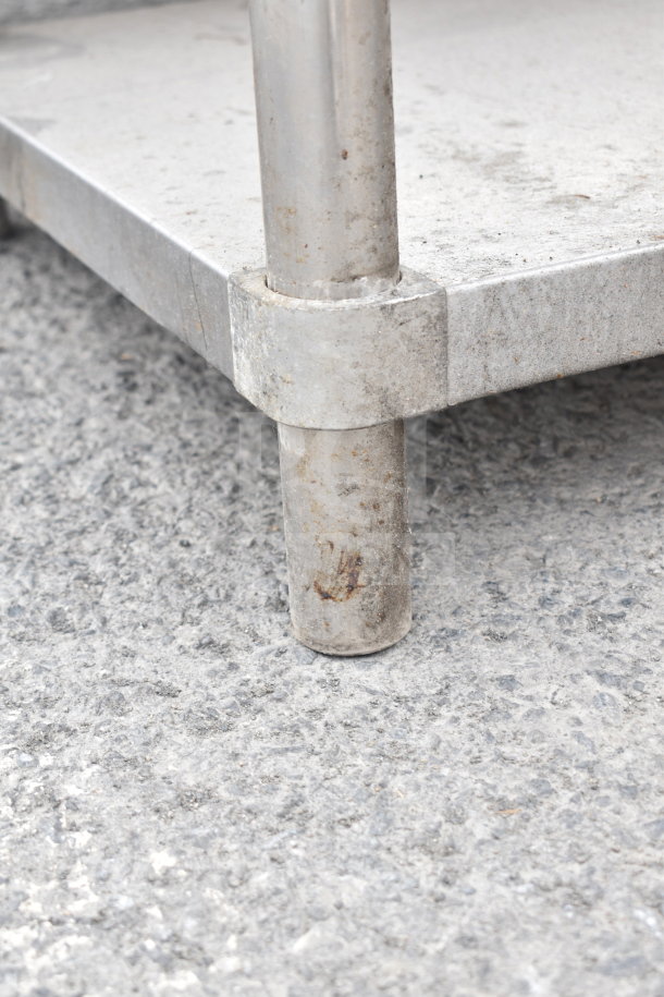 Metal table with an under shelf, showing signs of wear and rust, sturdy design with round legs and a square base.