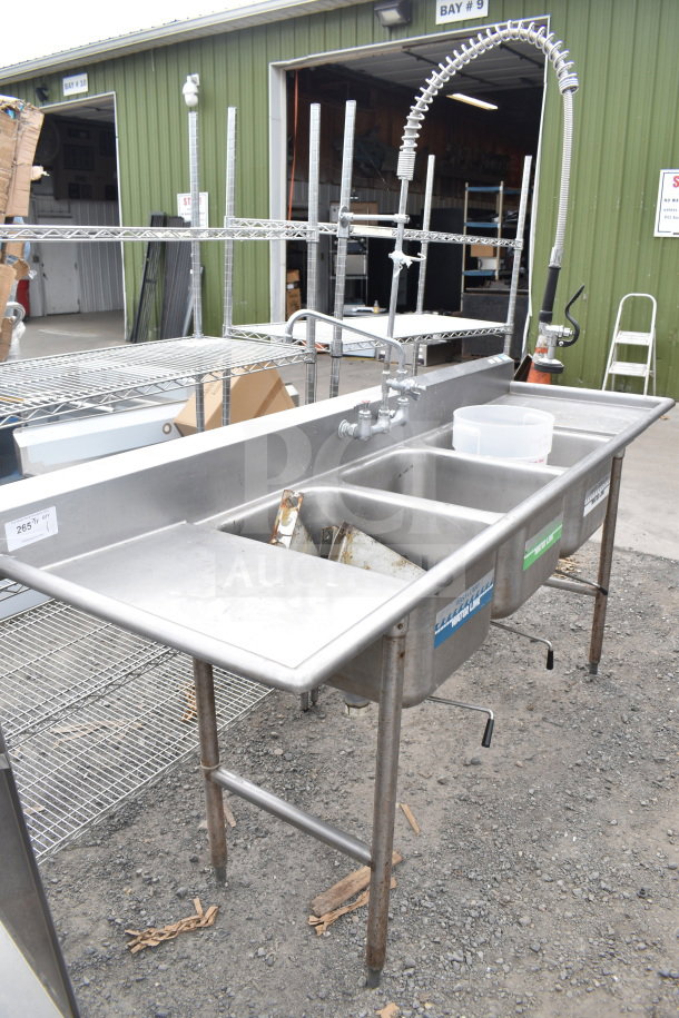Commercial 3 bay sink with dual drain boards, faucet, and spray nozzle. Stainless steel, durable, used condition.