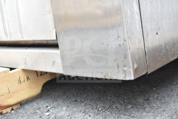 Commercial gas-powered single deck pizza oven, stainless steel, visible wear. Image shows corner detail and wooden pallet support.