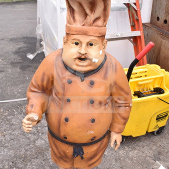 Lifesize chef statue in orange uniform and hat, holding a spoon. Slight wear visible. Unique decor item for kitchens.