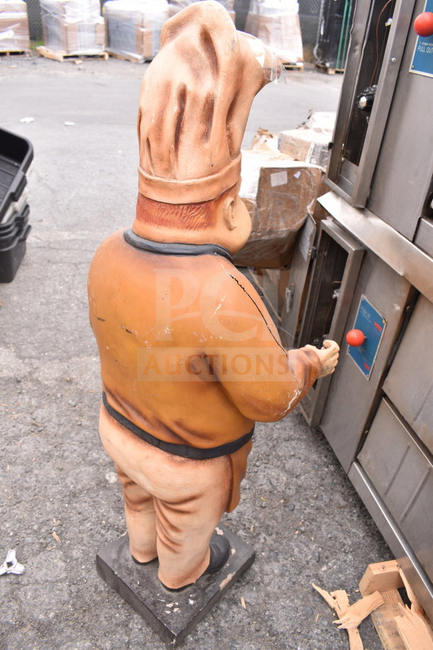 Large chef statue with a white hat and orange uniform, showing signs of wear and cracks. Ideal for restaurant decor.