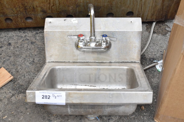 Commercial single bay wall mount sink with faucet and handles, stainless steel, shows moderate wear, label indicating item number 282.