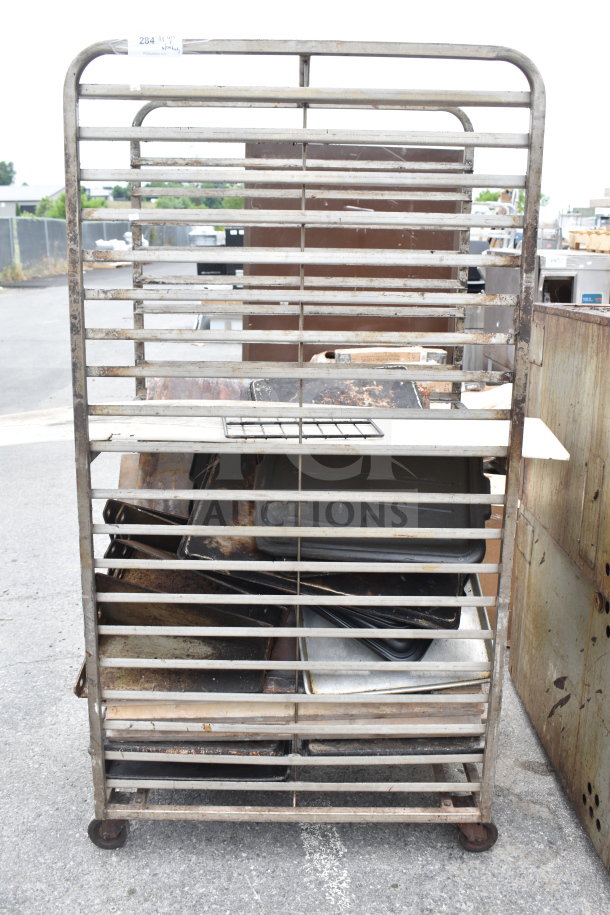 Commercial pan transport rack with multiple shelves, on sturdy commercial casters, visible wear and rust.