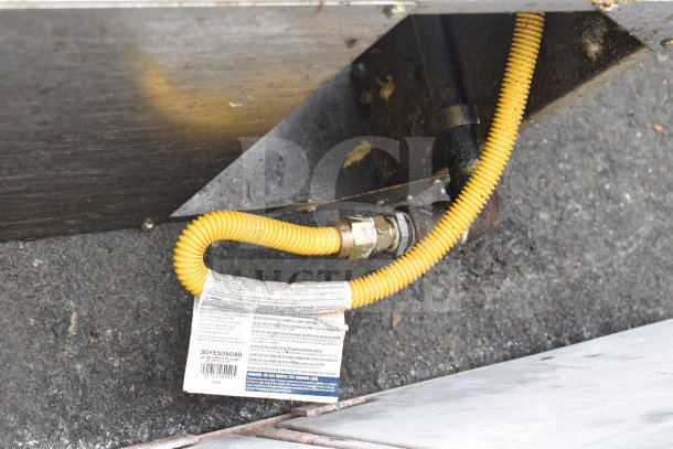 Commercial gas-powered floor style deep fat fryer, featuring a yellow gas line and visible safety label with serial number 30YE505048.