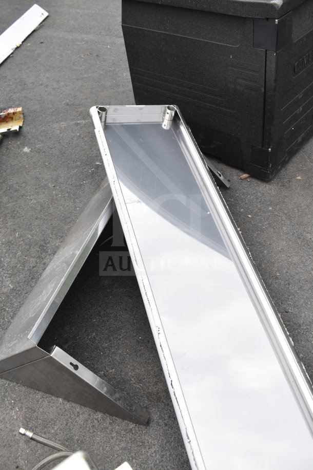 Two metal shelves with stainless steel finish, used condition, lying on a concrete floor.