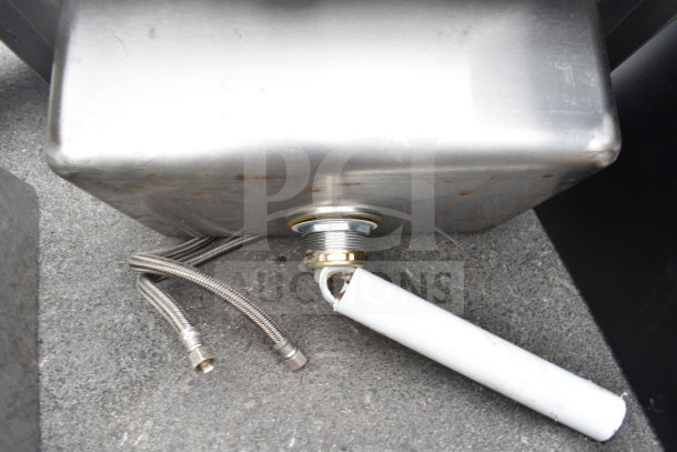 Commercial single bay wall mount sink with visible faucet connections and handles, stainless steel, slight wear.