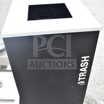 Black trash bin with a white top and "TRASH" label on the side. Shows minor surface scuffs.