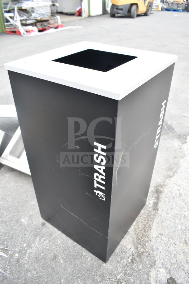 Black trash bin with square opening and "TRASH" label on side. Minor surface marks, sturdy condition. Ideal for outdoor use.