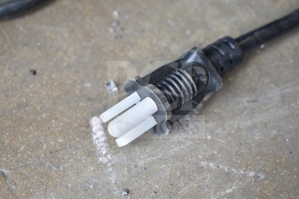 Close-up of a power plug on a concrete surface, associated with a KoolMore Merchandiser.