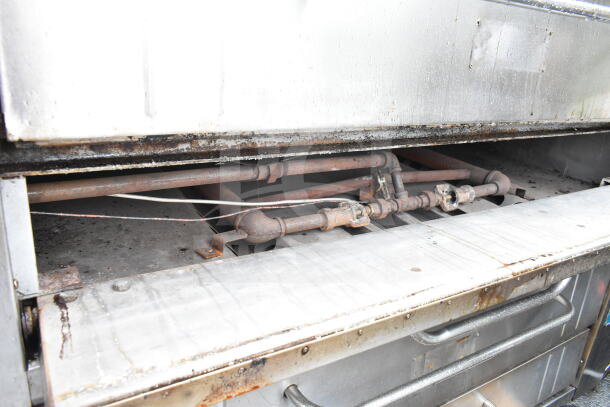 Commercial gas-powered single deck pizza oven, shows interior burner and piping, steel construction with signs of use.