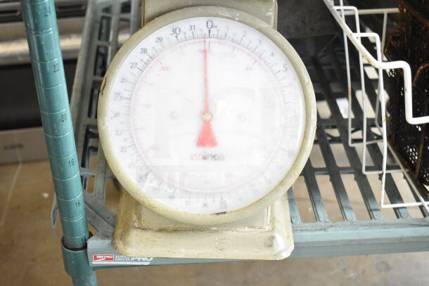 Winco SCLH-2 countertop scale with white dial and red needle, in used condition on a metal shelf.