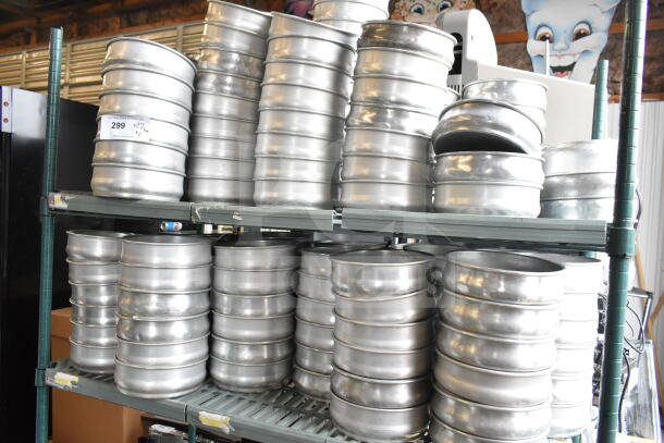 Lot of round metal baking pans stacked in two tiers on shelves. Made of durable metal, ideal for commercial use.