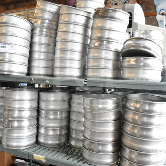 Lot of round metal baking pans stacked in two tiers on shelves. Made of durable metal, ideal for commercial use.
