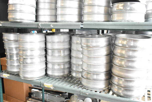 Lot of round metal baking pans in two tiers, shiny surface, stacked on metal shelving, good condition.