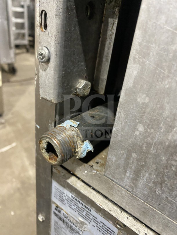 Close-up of rusted gas connection on Bakers Pride stainless steel 10-burner range, model 955394604036. Visible label with warning text.