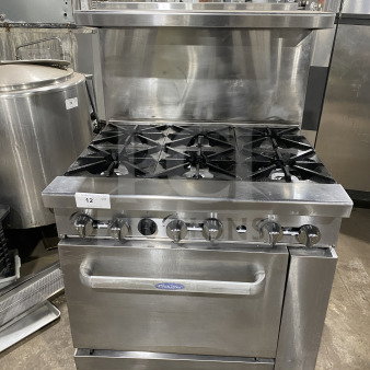 CookRite stainless steel 6-burner range/oven combo with backsplash, overhead salamander shelf, and wired oven rack, on casters.