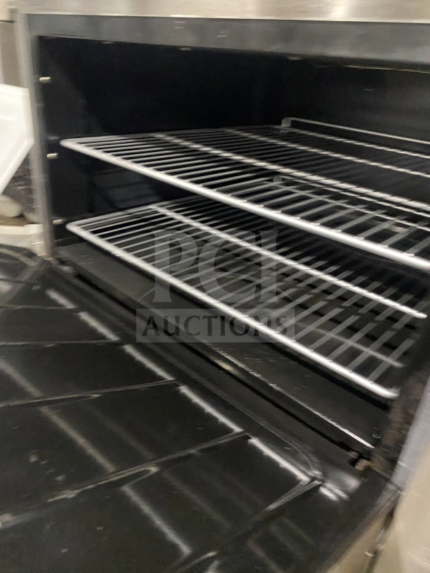 CookRite stainless steel gas 6-burner range/oven combo with backsplash, salamander shelf, and wired oven rack on casters.