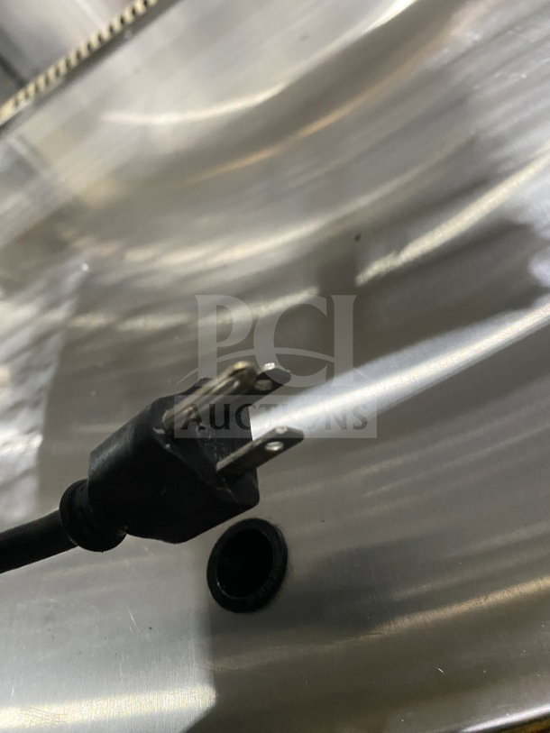 Leader EMCB48D 48" dry bakery display case plug view. Black power cable with plug, metal surface backdrop.