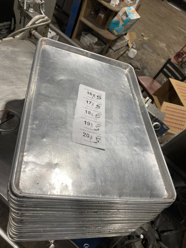 Stack of commercial stainless steel full-size baking sheet pans, lightly used condition, visible auction tag.