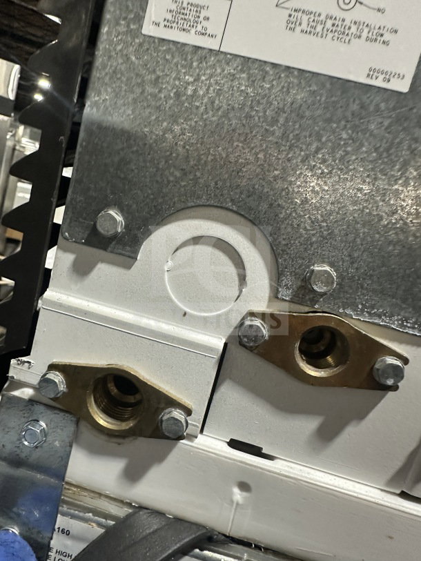 Close-up of Manitowoc ice machine connectors and metal plate, showing bolts and manufacturer's label with model and serial number.