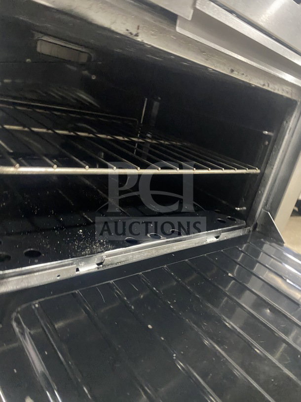 Commercial stainless steel 2-burner gas range with plancha grill, convection oven, wired rack, and splash back.