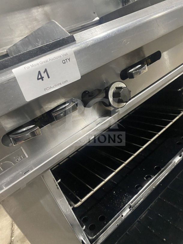 Commercial stainless steel gas-powered 2-burner range with plancha grill, convection oven, wired rack, and splash back.