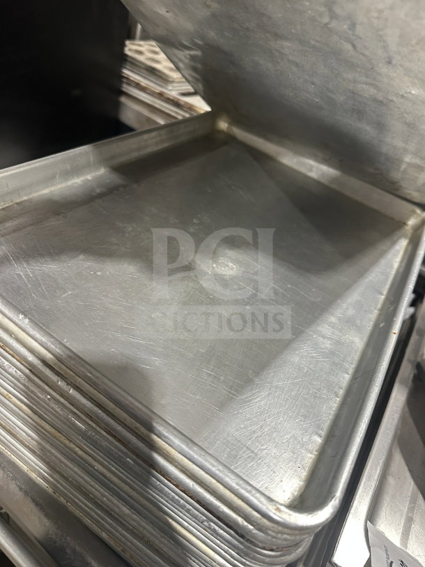 Stainless steel commercial baking sheet pan stack, used condition, showing minor surface wear. Auction item for bulk bidding.