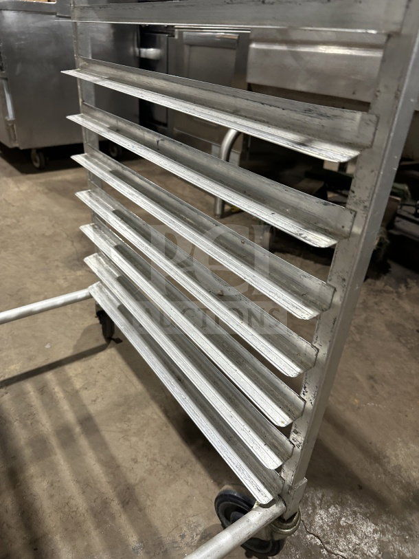 Commercial stainless steel pan rack on casters, small-size, heavy-duty condition, for sheet/bun pans, visible wear.