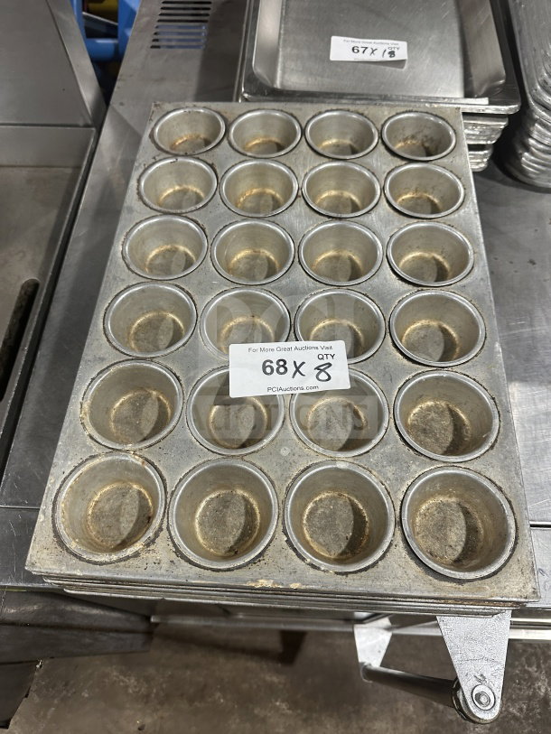 Commercial heavy-duty stainless steel 24-cup muffin pan, used condition, stack of eight with auction label visible.