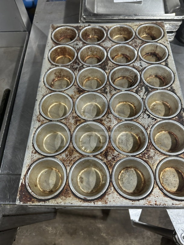 Commercial 24-cup stainless steel muffin pan, heavy-duty, used condition, visible wear and staining, ideal for bulk baking.