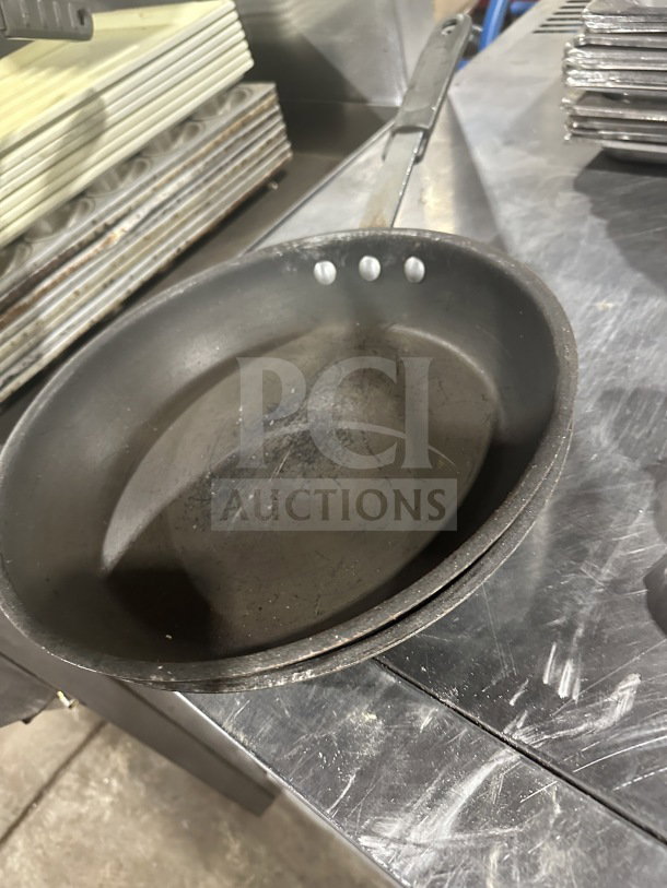 Commercial heavy-duty aluminum non-stick frypan, slightly worn. Features riveted handle, ideal for professional kitchens.