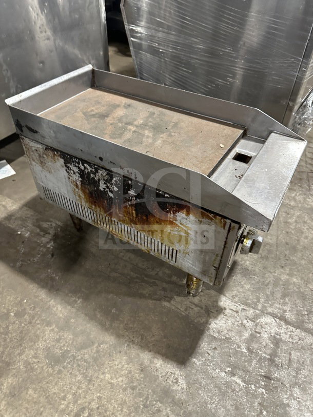 Commercial stainless steel gas-powered countertop flat top griddle on legs, showing signs of wear and surface discoloration.